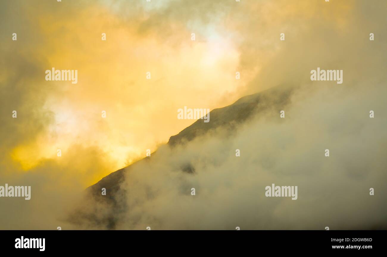 Sunlight breaking through dense storm clouds over a mountain ridge ...