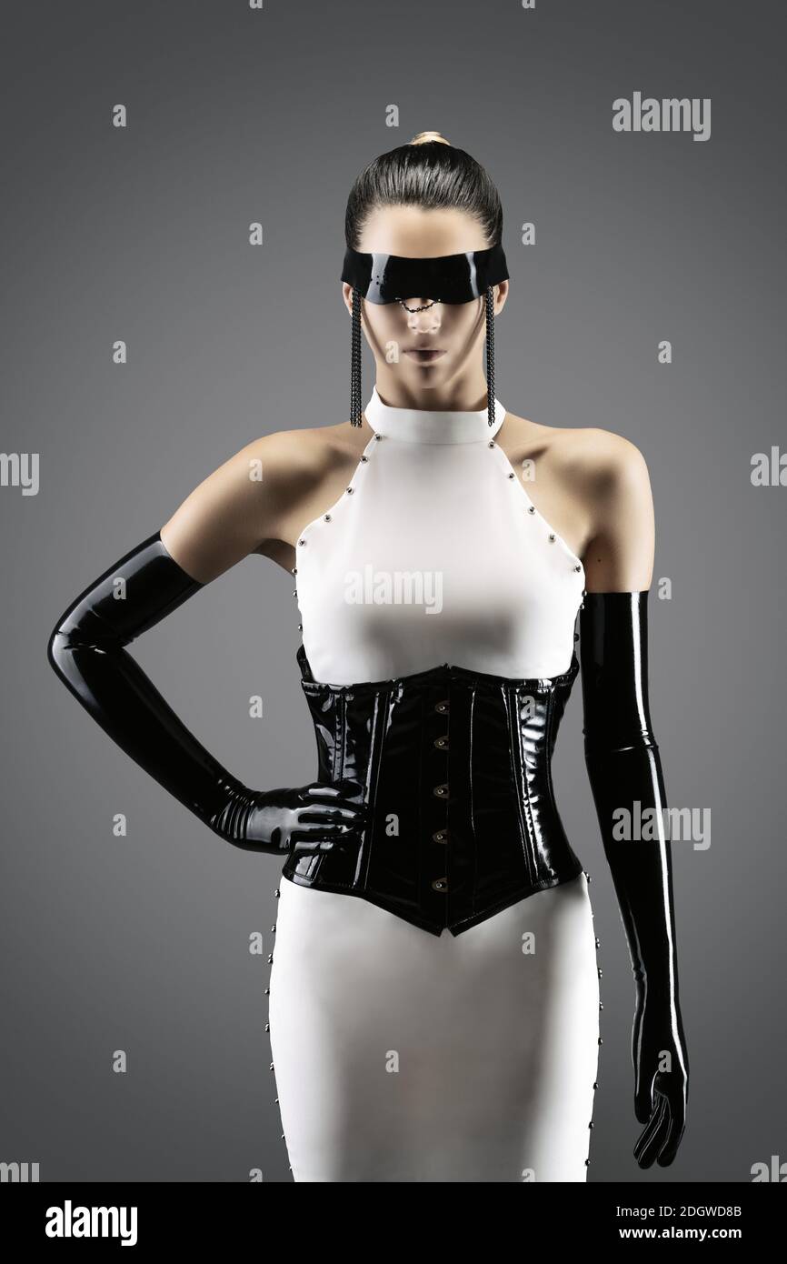 Futuristic portrait of a pretty young woman in a white dress, wearing a waist cincher, gloves and a black latex headband Stock Photo