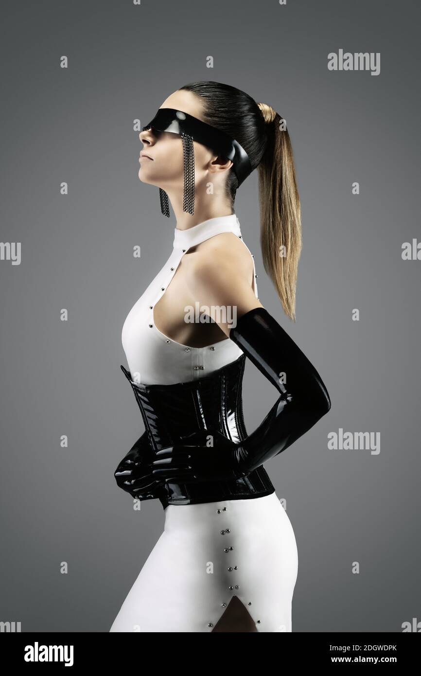 Futuristic portrait of a pretty young woman in a white dress, wearing a waist cincher, gloves and a black latex headband Stock Photo