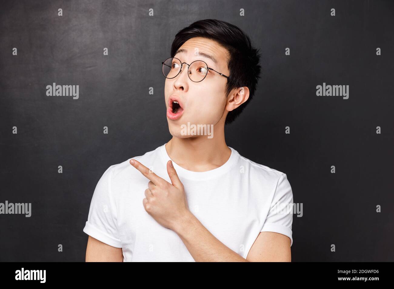 Close-up portrait of impressed asian handsome man in glasses and white t-shirt spot cool promo, open mouth wondered, pointing fi Stock Photo