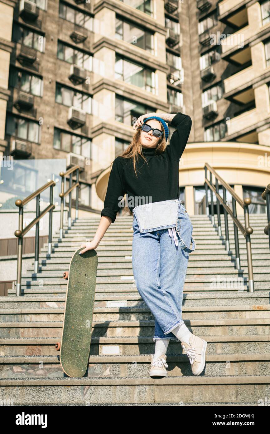 Stylishly dressed woman in blue denim jumpsuit posing with skateboard.  Street photo. Portrait of girl holding skateboard. Lifest Stock Photo -  Alamy