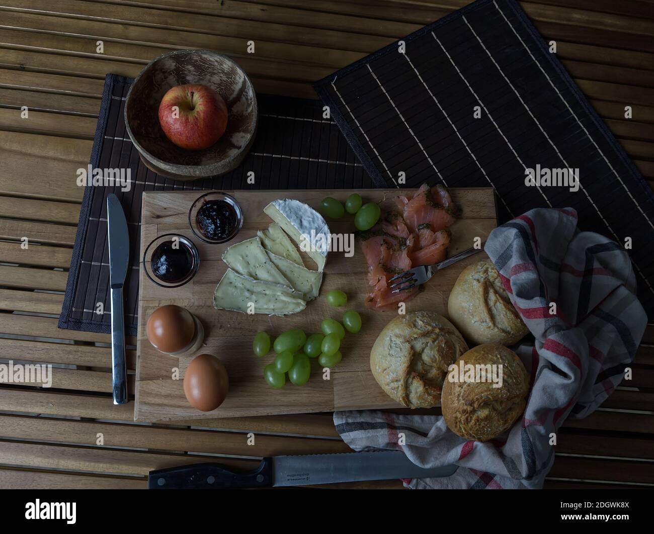 A tasty european breakfast with eggs, salmon, grapes, cheese and rolls