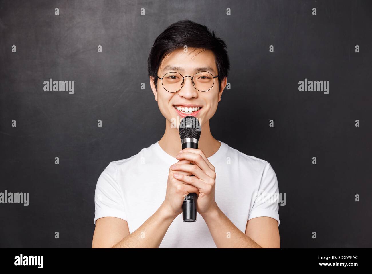 Leisure, people and music concept. Portrait of cute smiling asian man in white t-shirt, holding microphone both hands, singing s Stock Photo
