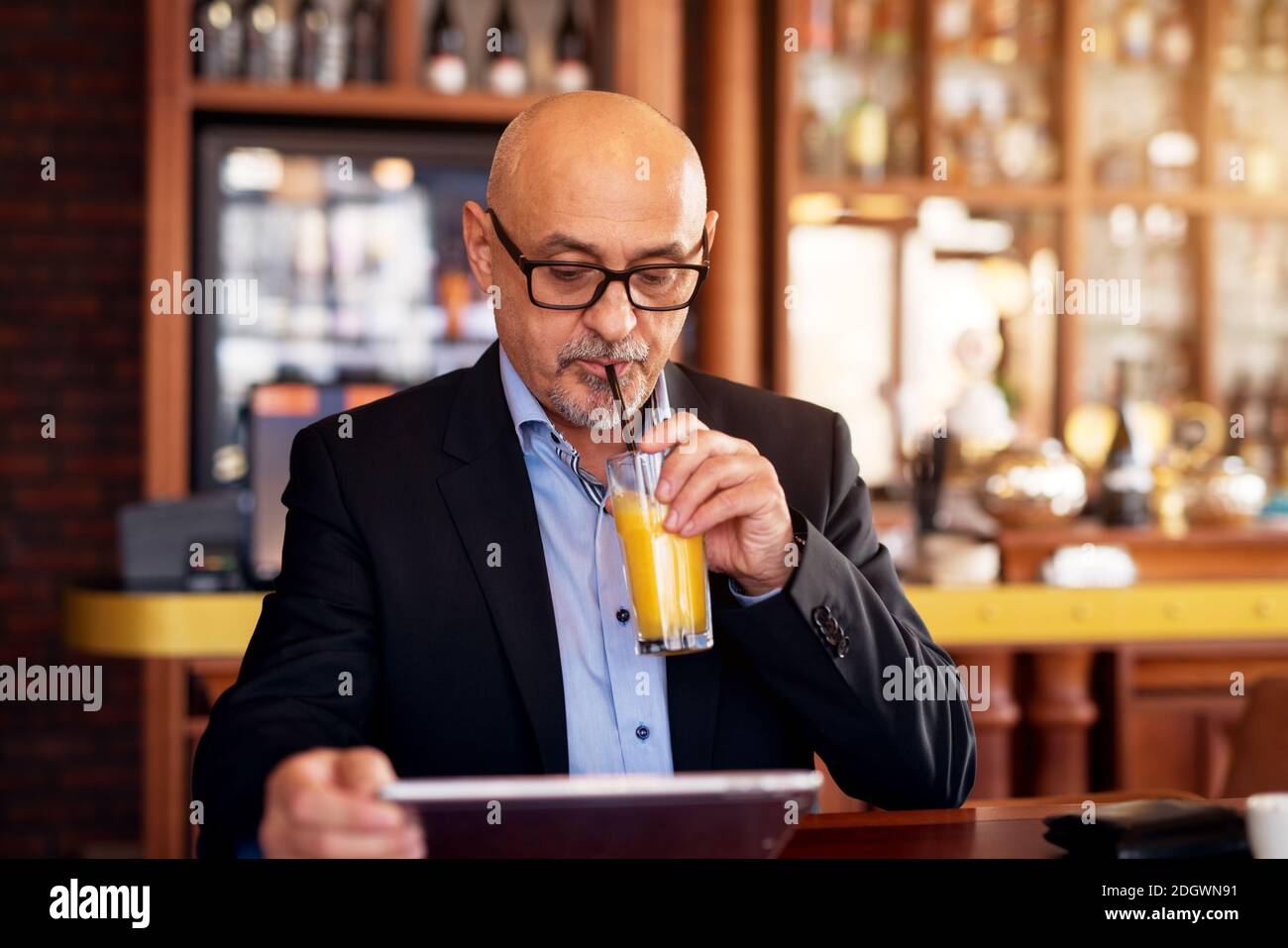 Mature Elegant Serious Businessman Is Using A Tablet And Drinking Juice