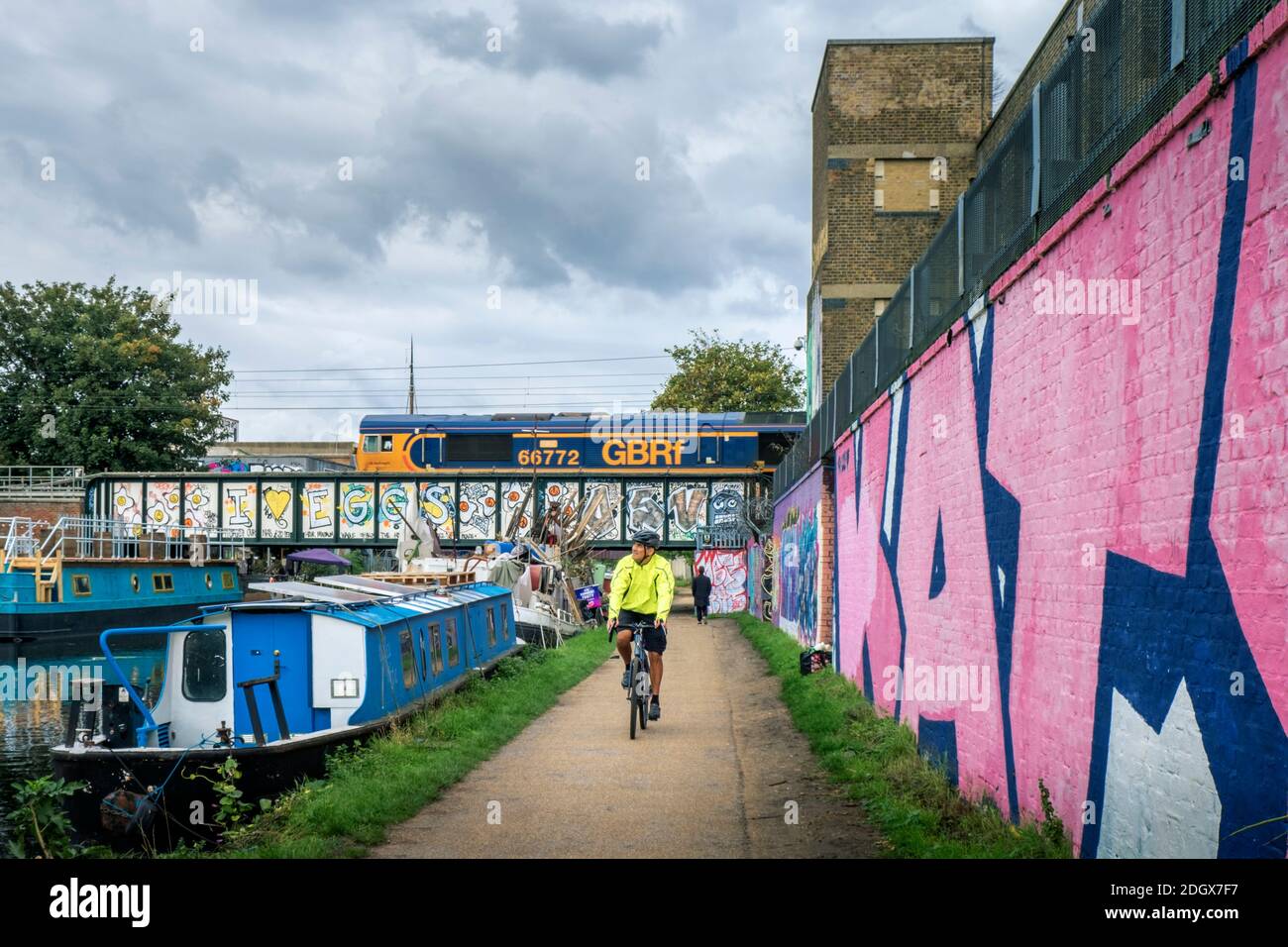 A cyclist on the Lea Valley towpath, GBRf freight train, houseboats, street art, Legacy Wharf, Stratford, East London, E15 2PN, UK Stock Photo
