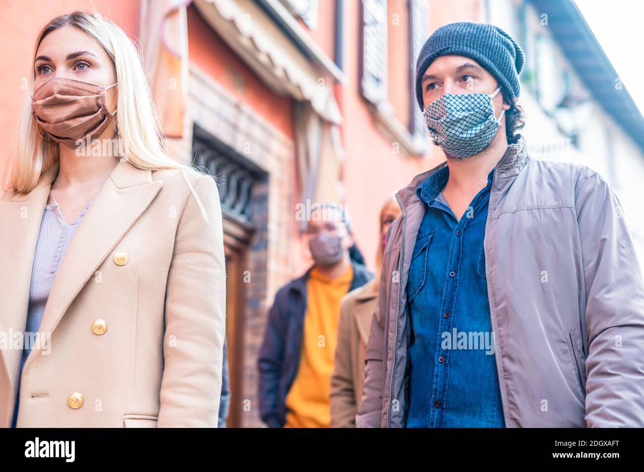Multiracial crowd walking near wall at city urban context - New normal lifestyle concept with young people covered by protective face mask - Selective Stock Photo