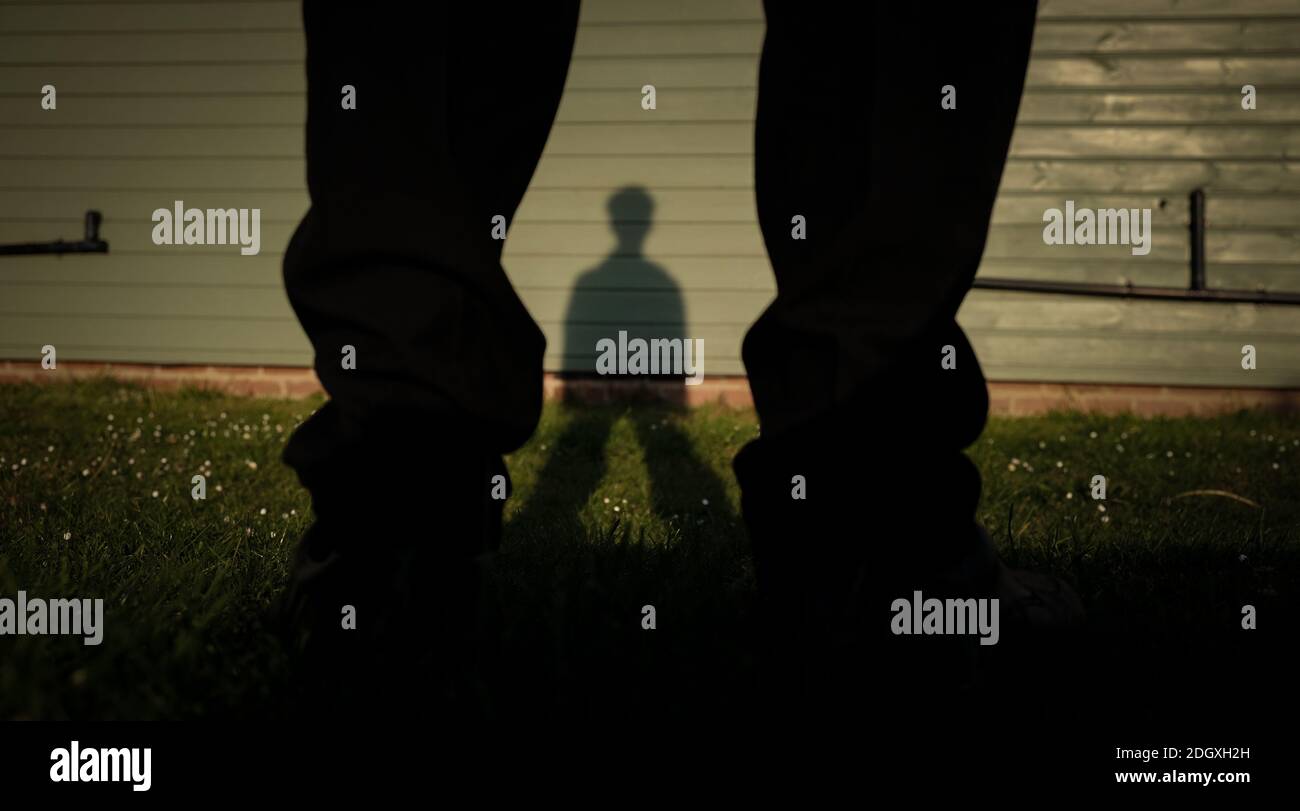 A boys legs with the shadow of his body being projected onto the grass and wooden slats for use in many concepts. Stock Photo