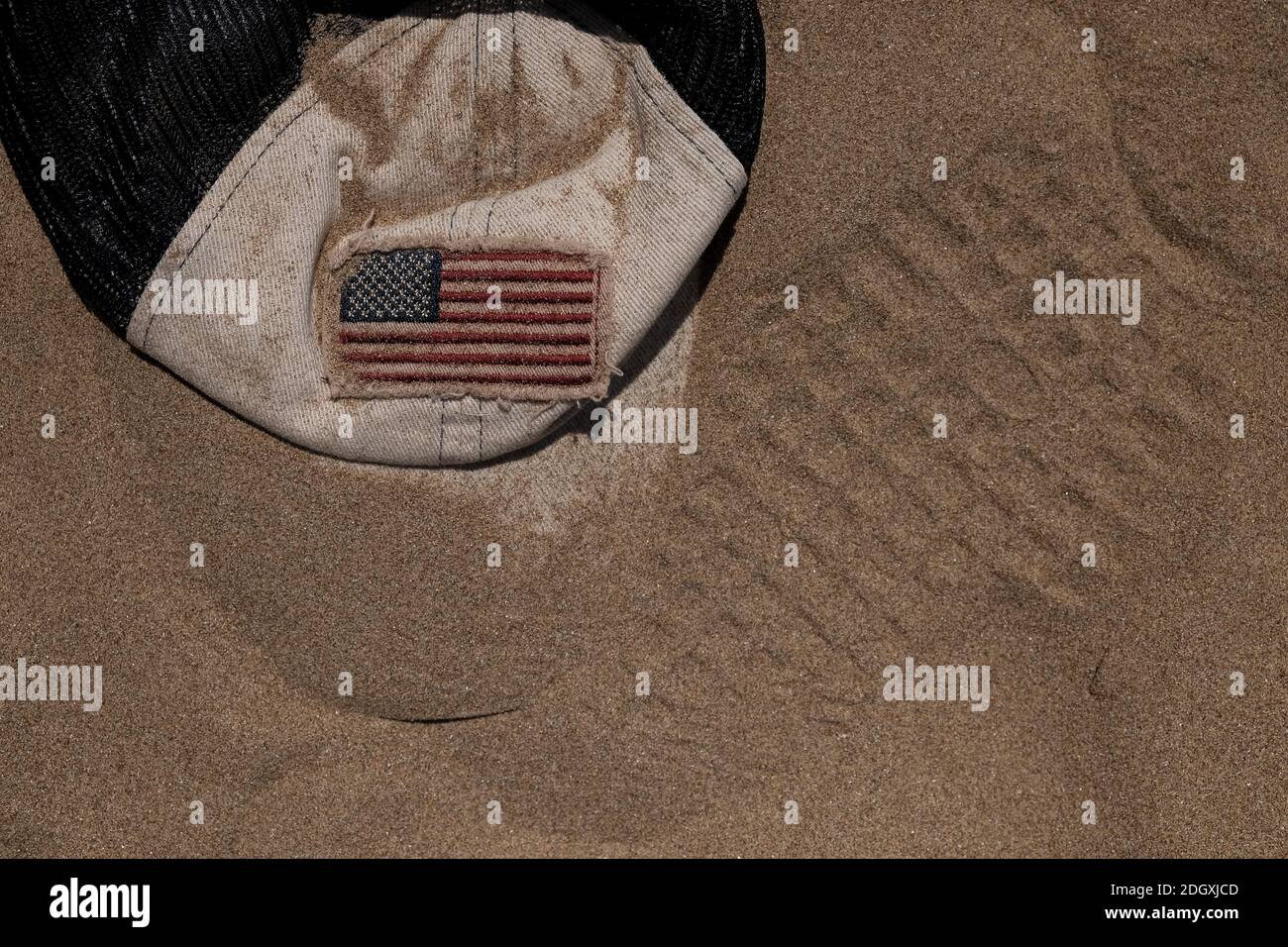 American flag on a baseball cap that is buried in the sand, could be used as a concept image for moon exploration. Stock Photo