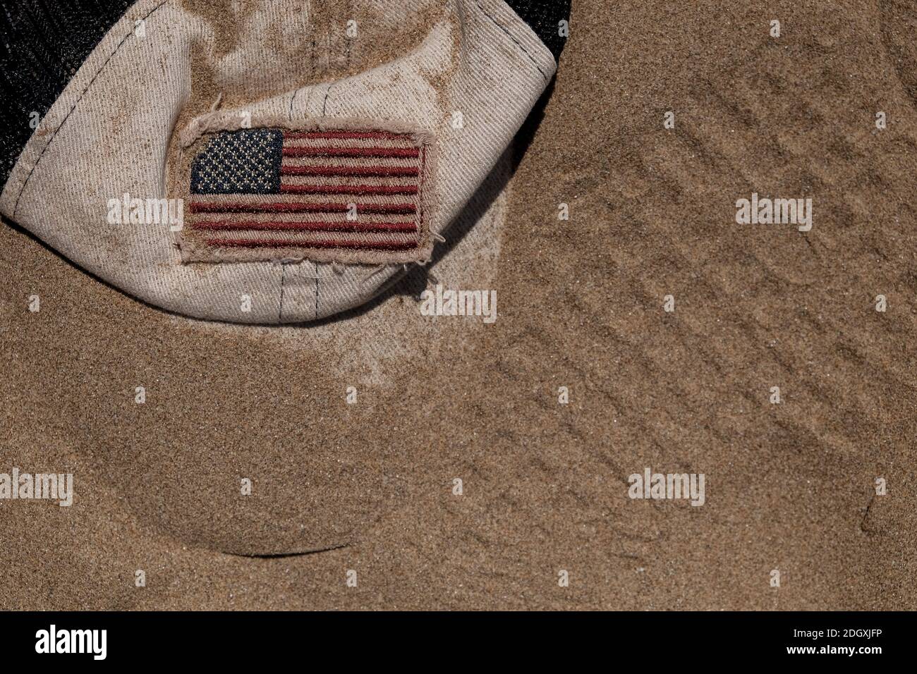 American flag on a baseball cap that is buried in the sand, could be used as a concept image for moon exploration. Stock Photo