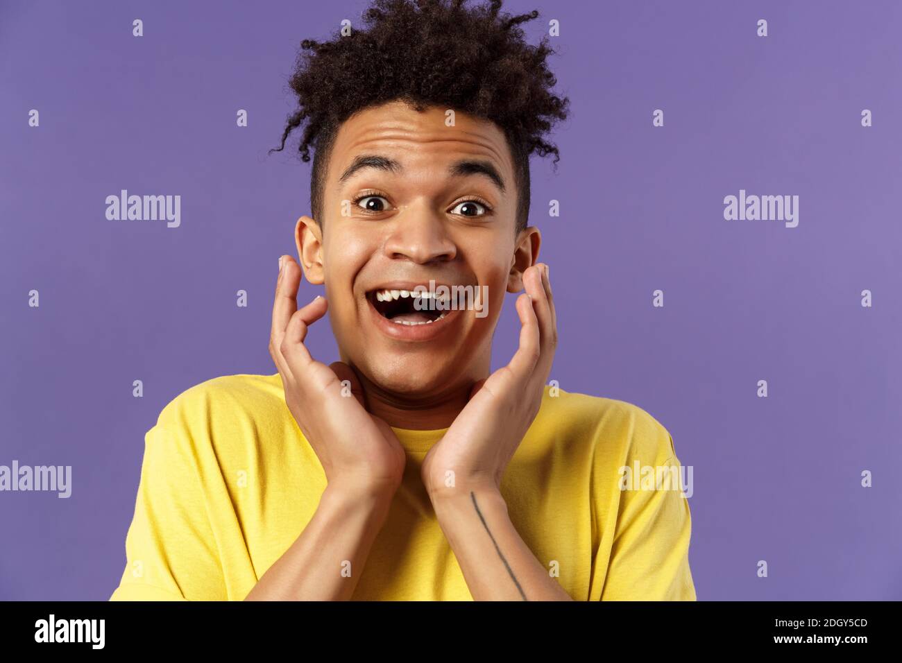 Close-up portrait of extremely happy, enthusiastic young man hear fantastic news, looking surprised and excited, touching face i Stock Photo