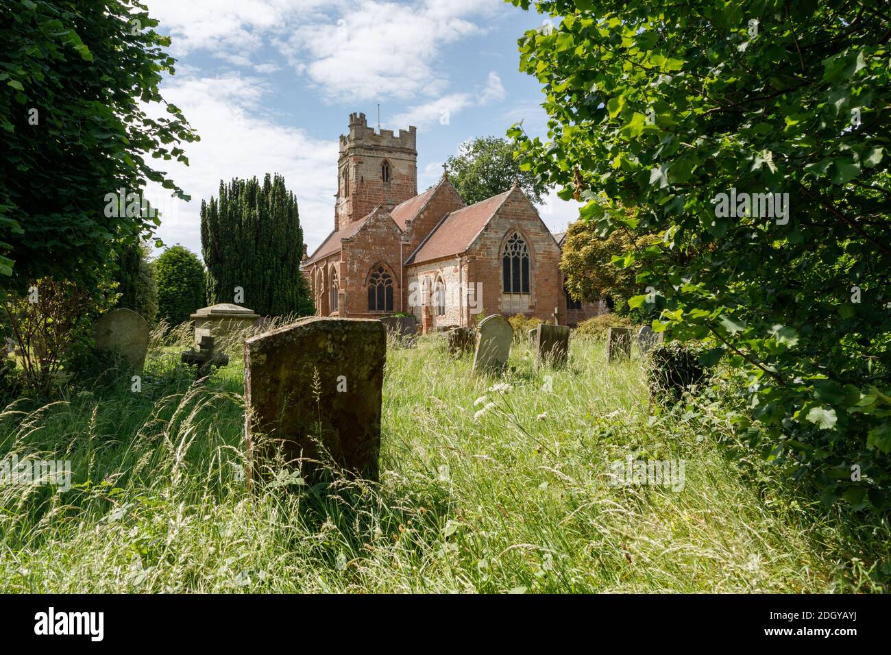 Dunchurch, Warwickshire, UK - 16/06/20: St. Peter's church in a partly overgrown churchyard from which old, stone gravestones stand in long grass. Stock Photo