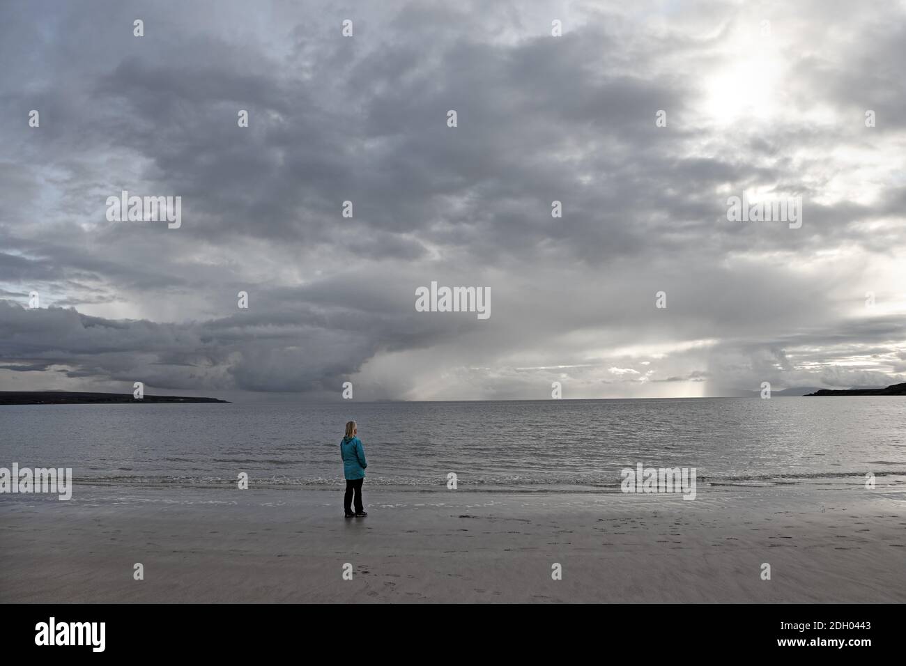 Woman on a Deserted Beach Looking Towards Clearing Storm Clouds on the Horizon, Sands Bay, Gairloch, Scotland, UK Stock Photo