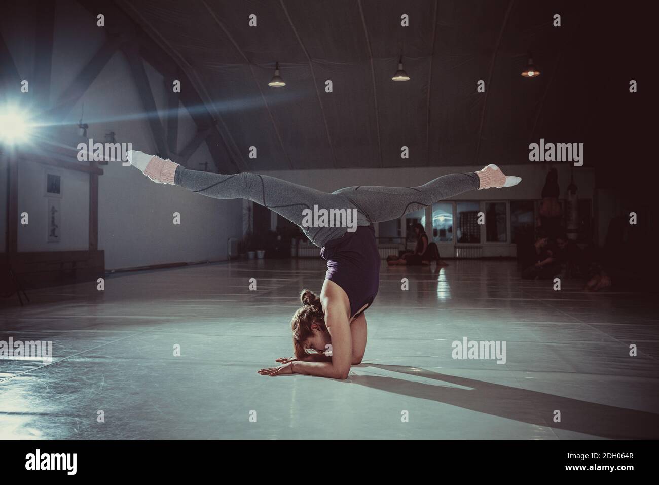 Young attractive yogi woman practicing yoga concept, standing in variation of Pincha Mayurasana exercise, handstand pose, workin Stock Photo