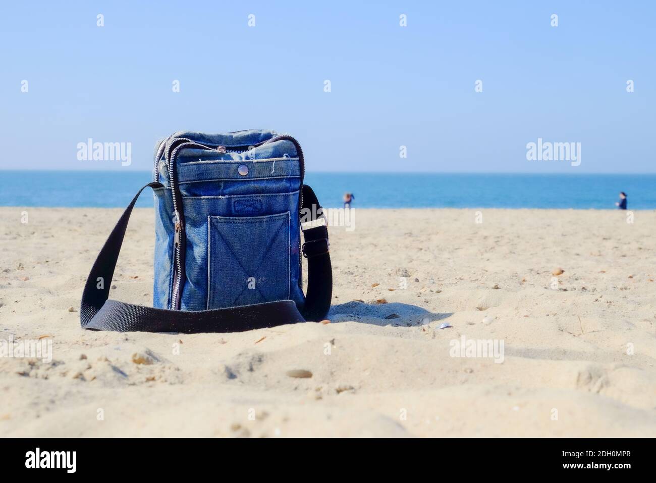 Blue denim bag with black strap on sandy beach Stock Photo