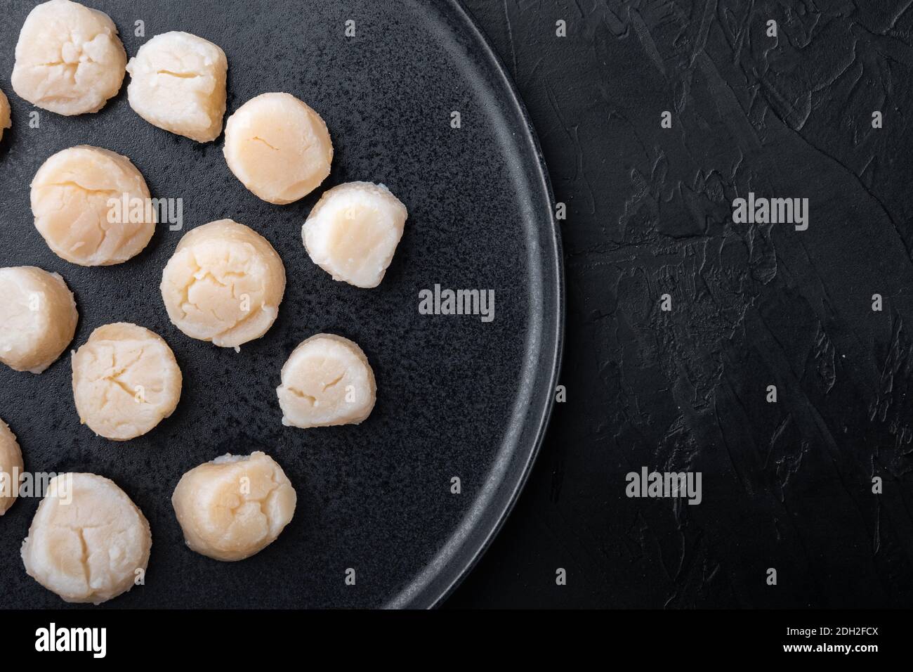 Fresh raw uncooked scallops, top view, on black textured background