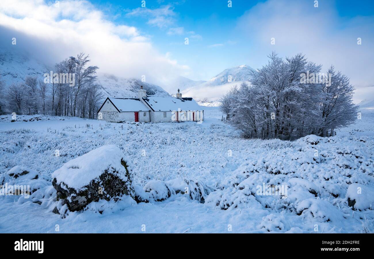 Snow covered Blackrock Cottage with mist covered Buachaille Etive Mor in the distance in winter, Glen Coe , Scotland, UK Stock Photo