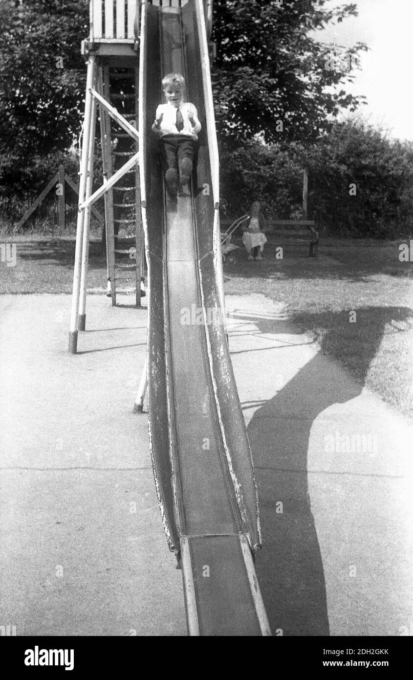 1960s, historical, outside at a playground, a young schoolboy coming down a traditional metal