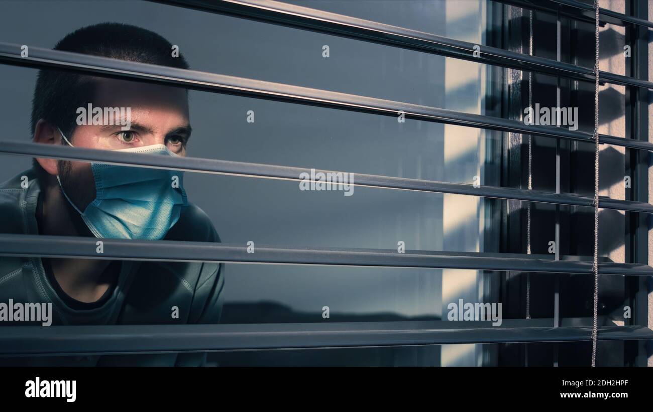 Coronavirus lockdown. Man with face mask looking through window. Stock Photo