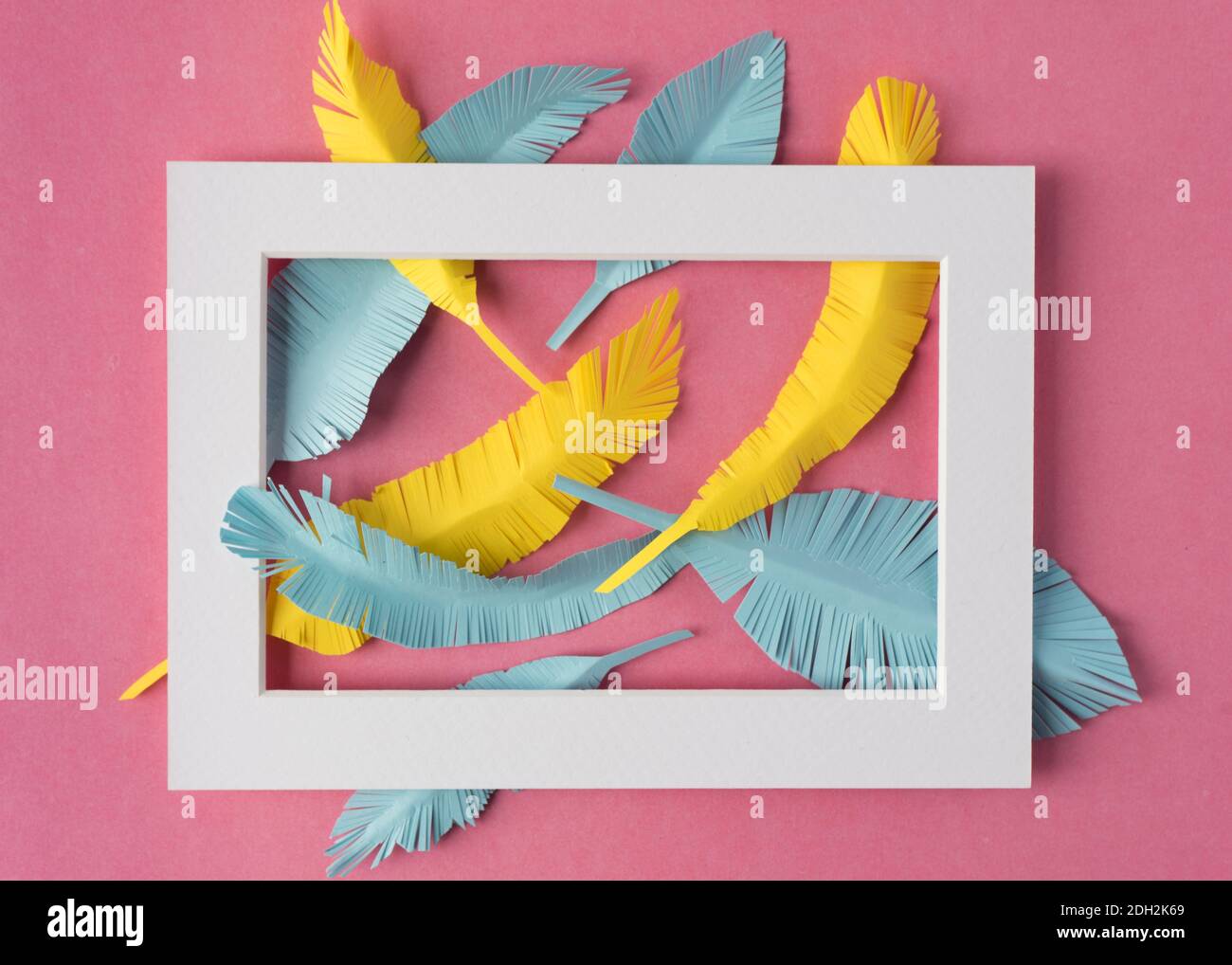 white frame with yellow and blue paper feathers on pink colorful background with copy space Stock Photo