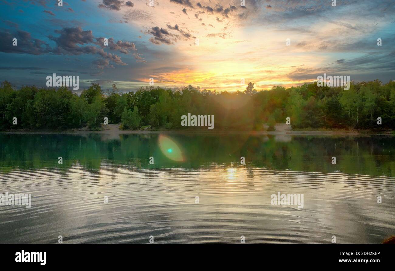 Dramatic sunset over a body of water surrounded by trees Stock Photo ...