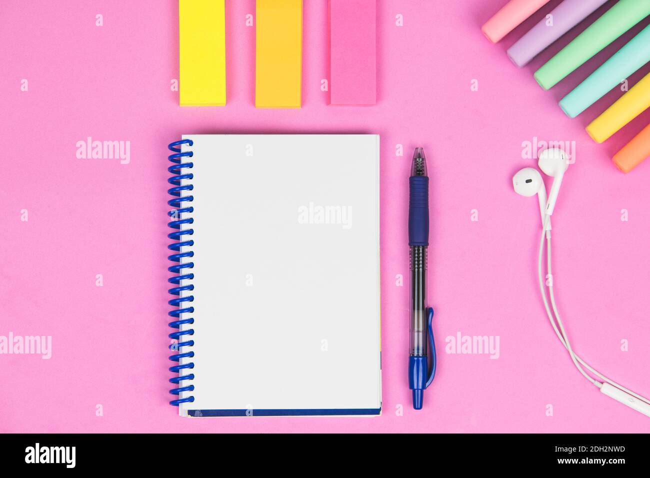 blank notebook on a pink background with pen, colored post, headphones and colored markers Stock Photo