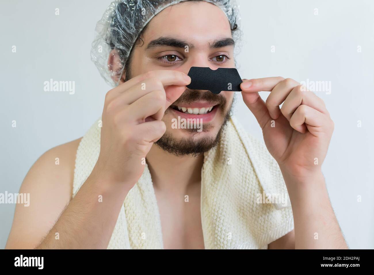 A young Caucasian man doing facial cleaning, removing whiteheads or blackheads on nose using pore strips Stock Photo