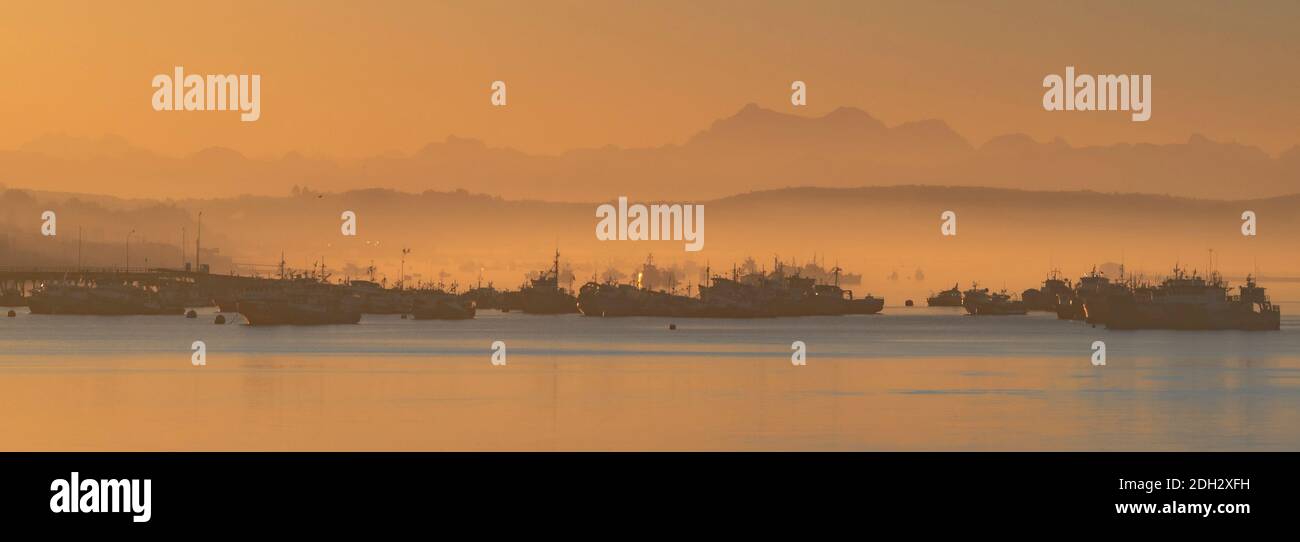 panoramic view of fishing boats in the mist of sunrise with mountains in the background Chiloe Stock Photo