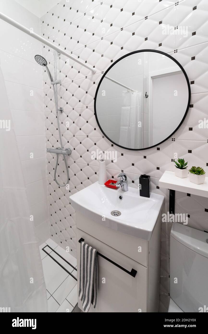 Part of a small modern stylish white black bathroom in the attic of an old house apartment with a sink on the cabinet and a round mirror Stock Photo