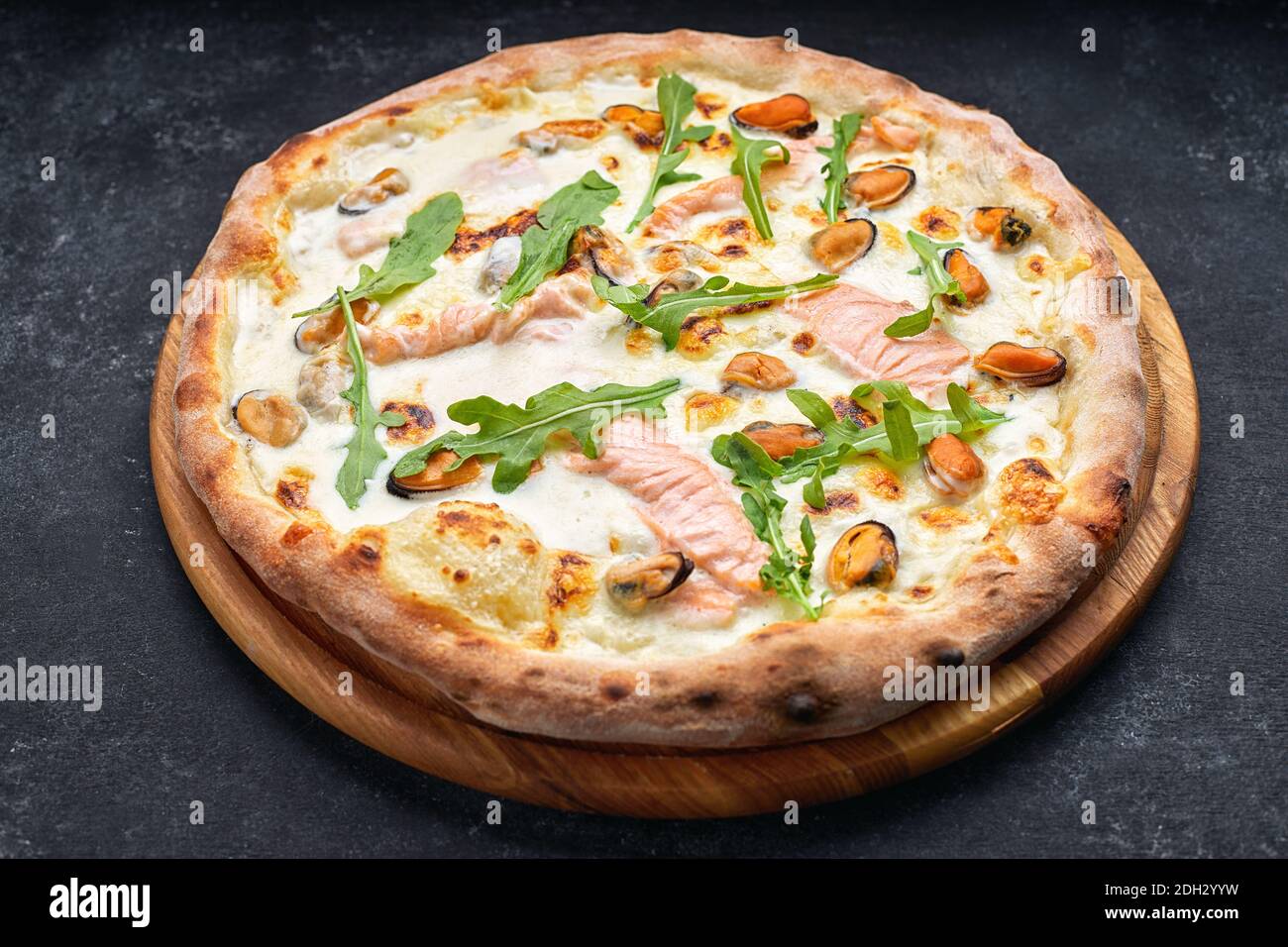 Seafood pizza, marinara, di mare, with salmon, mussels and arugula, on a wooden board, against a dark background Stock Photo