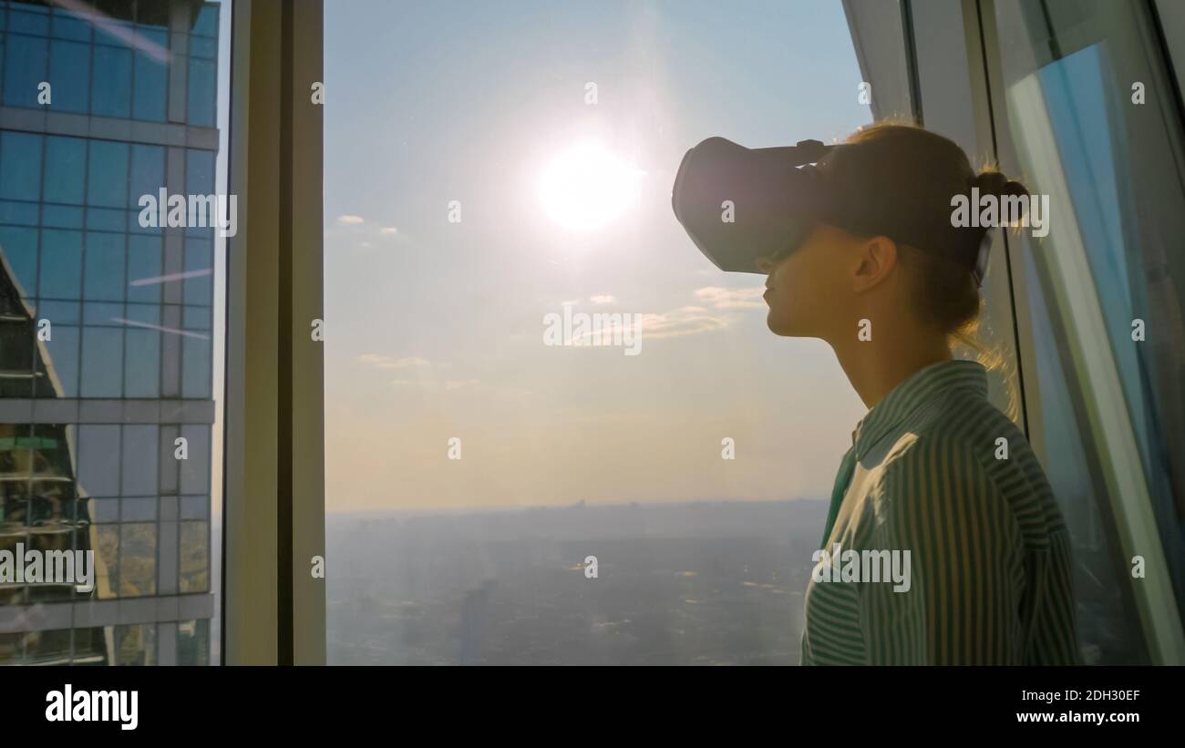 Young woman using virtual reality headset against skyscraper window - VR concept Stock Photo