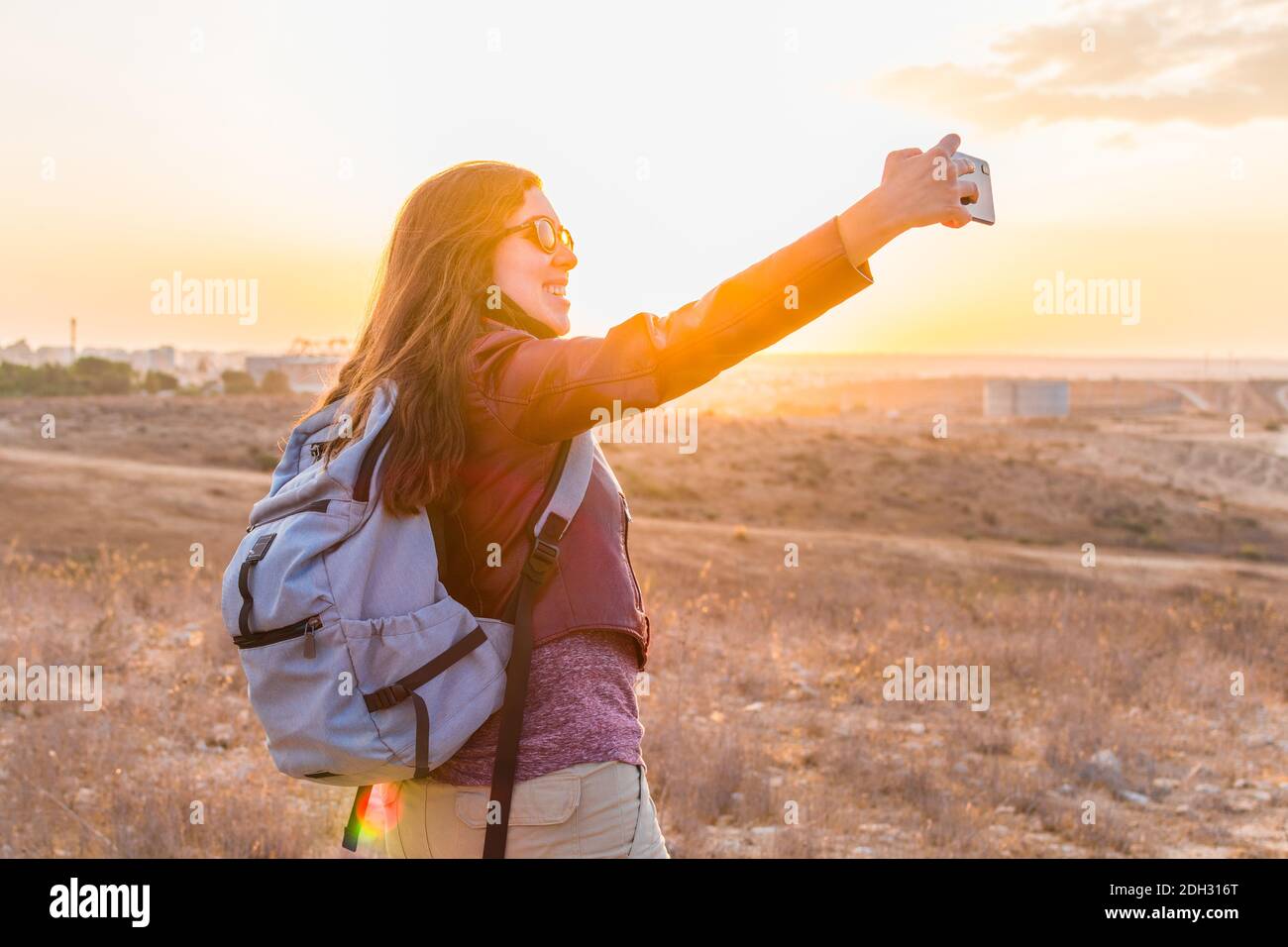 A young woman taking a selfie, while walking through the field at sunset. Stock Photo