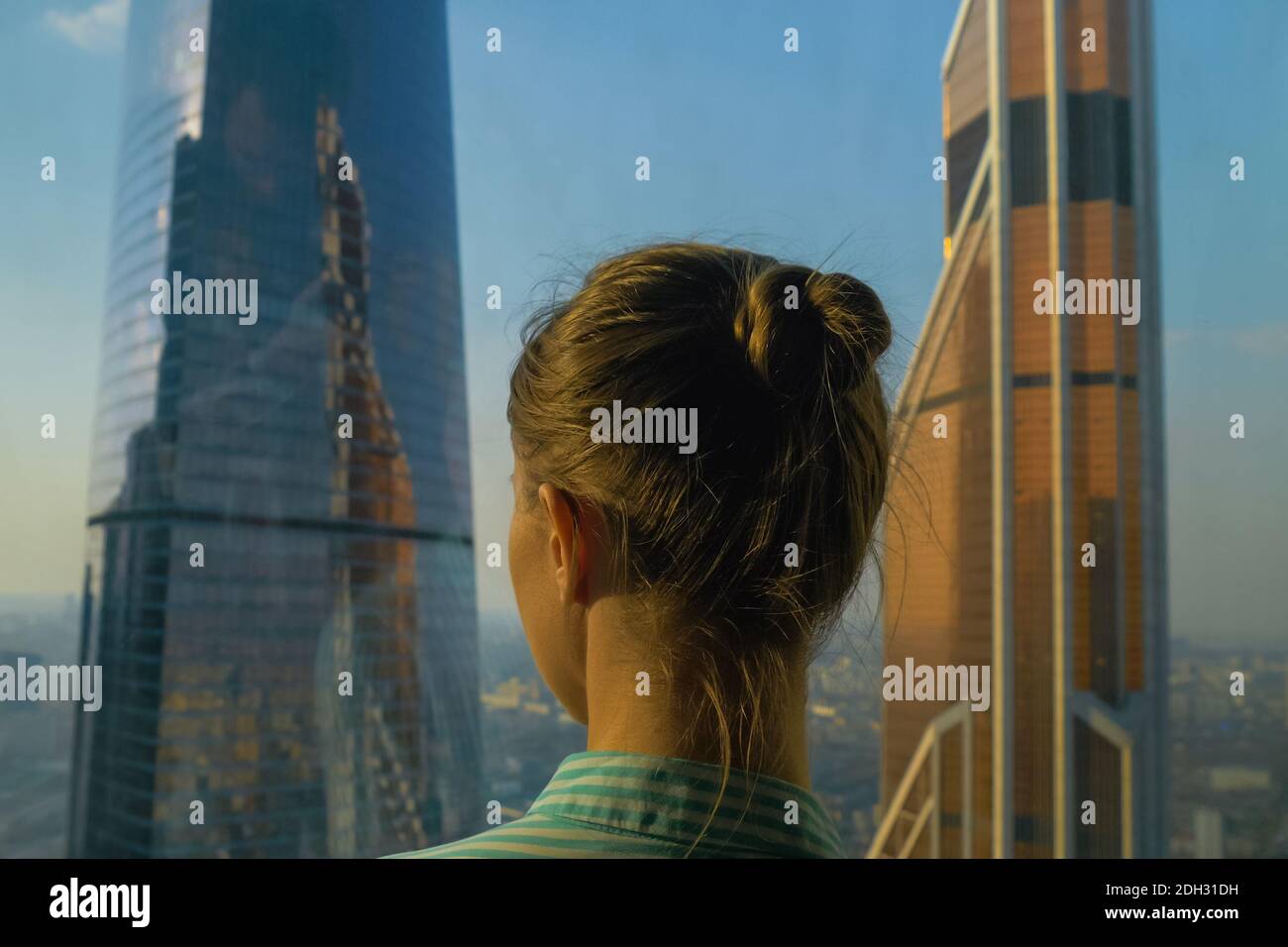 Back view of woman looking at cityscape through window of skyscraper ...