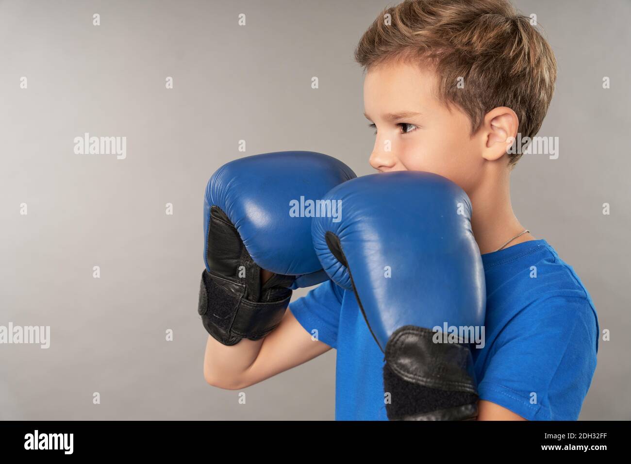 Adorable boy boxer wearing sports boxing gloves and blue shirt while