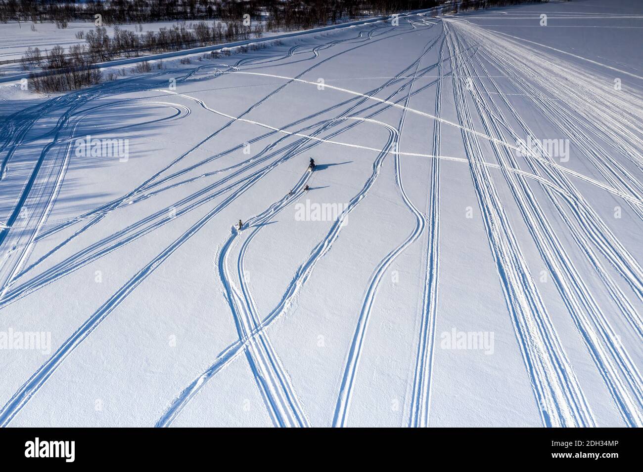 Scenic aerial view on adult driver pulled two children on snow racers with snowmobile, one child fall into snow - lost pulling rope. Holiday activity, Stock Photo