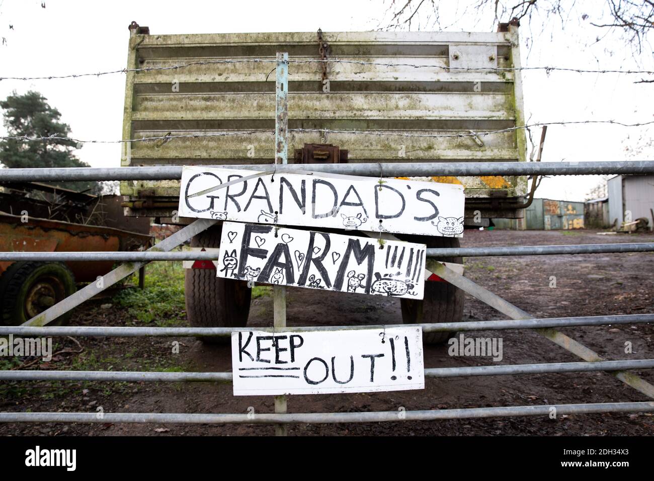 A sign to the entrance of a farm warning 'Keep out' 'Grandad's Farm' The gate is padlocked and surrounded with barbed wire. Stock Photo