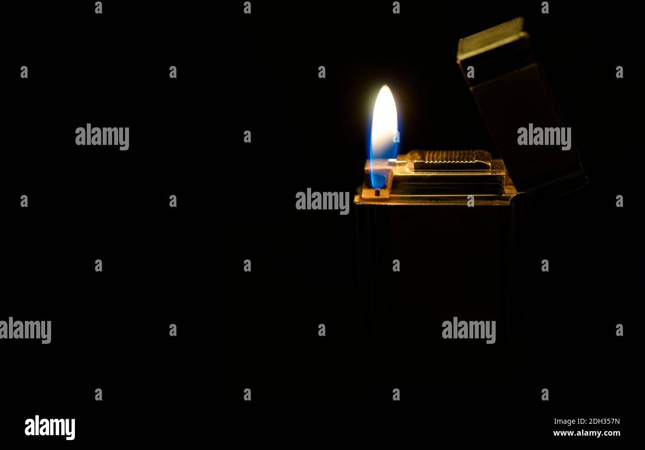 A flame against a dark background. An old and often used silver colored lighter glowing gold. Stock Photo