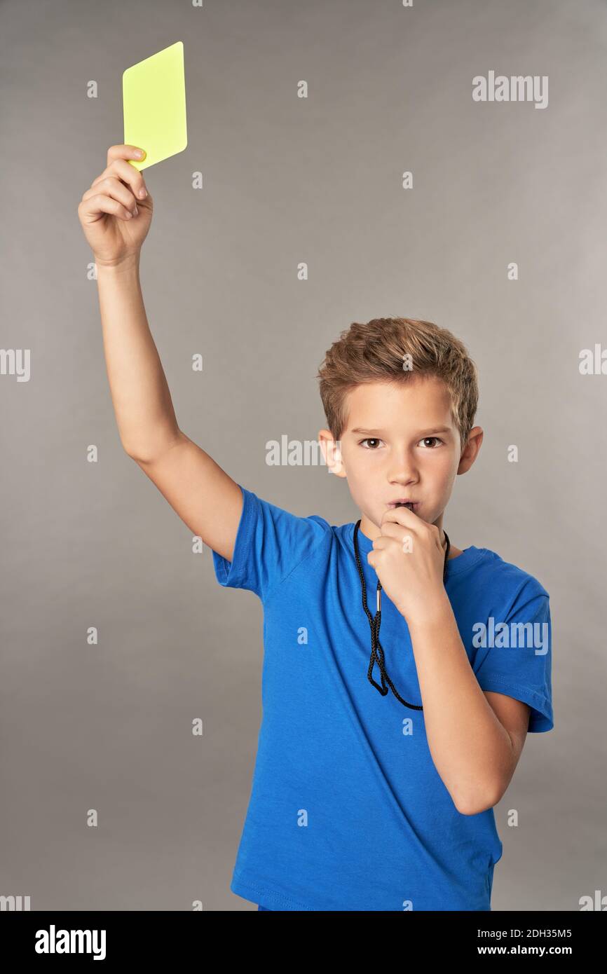Cute male child whistling and showing penalty card while standing against gray background Stock Photo