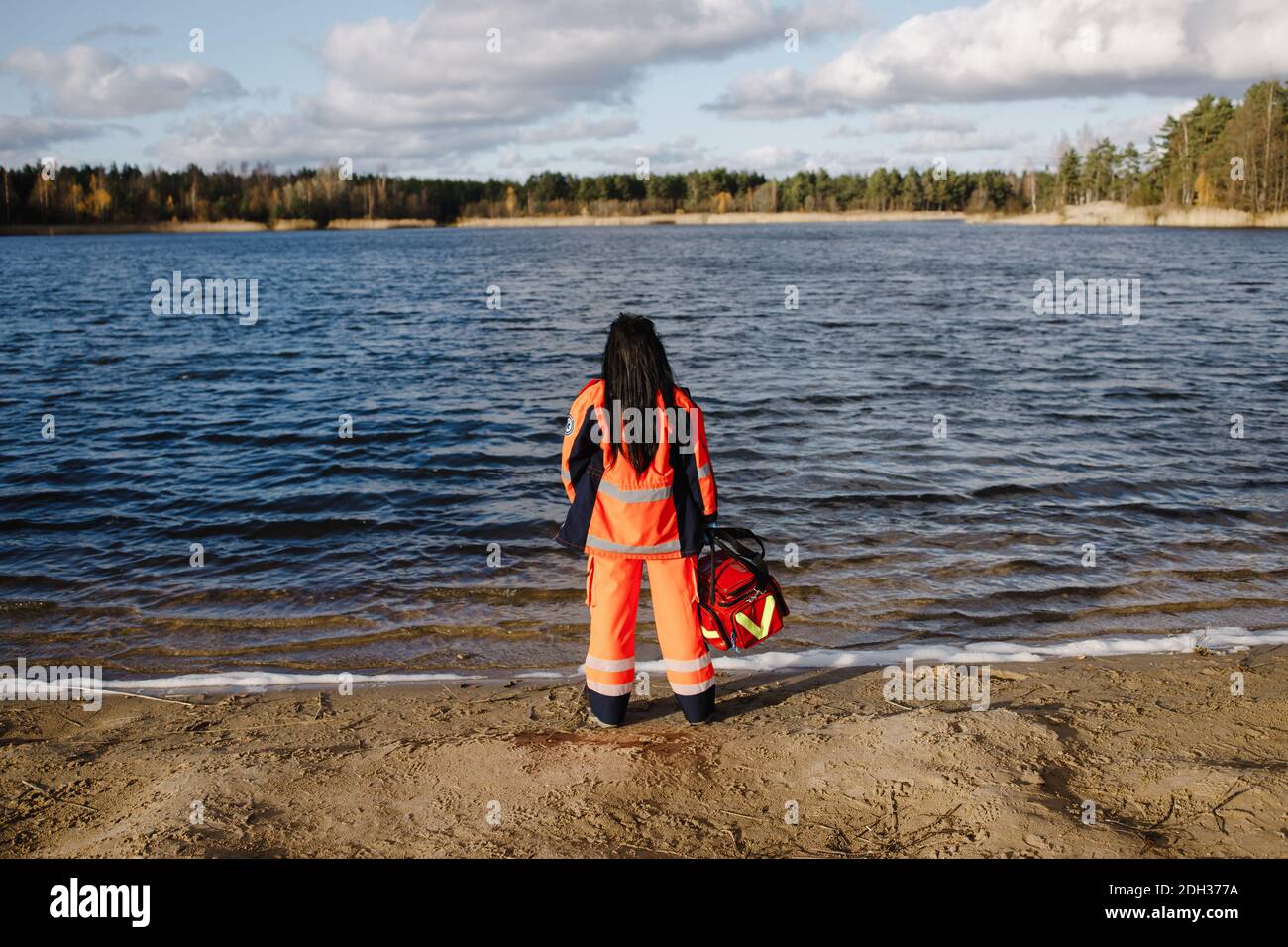 Female paramedic posing near blue lake on sunny day Stock Photo