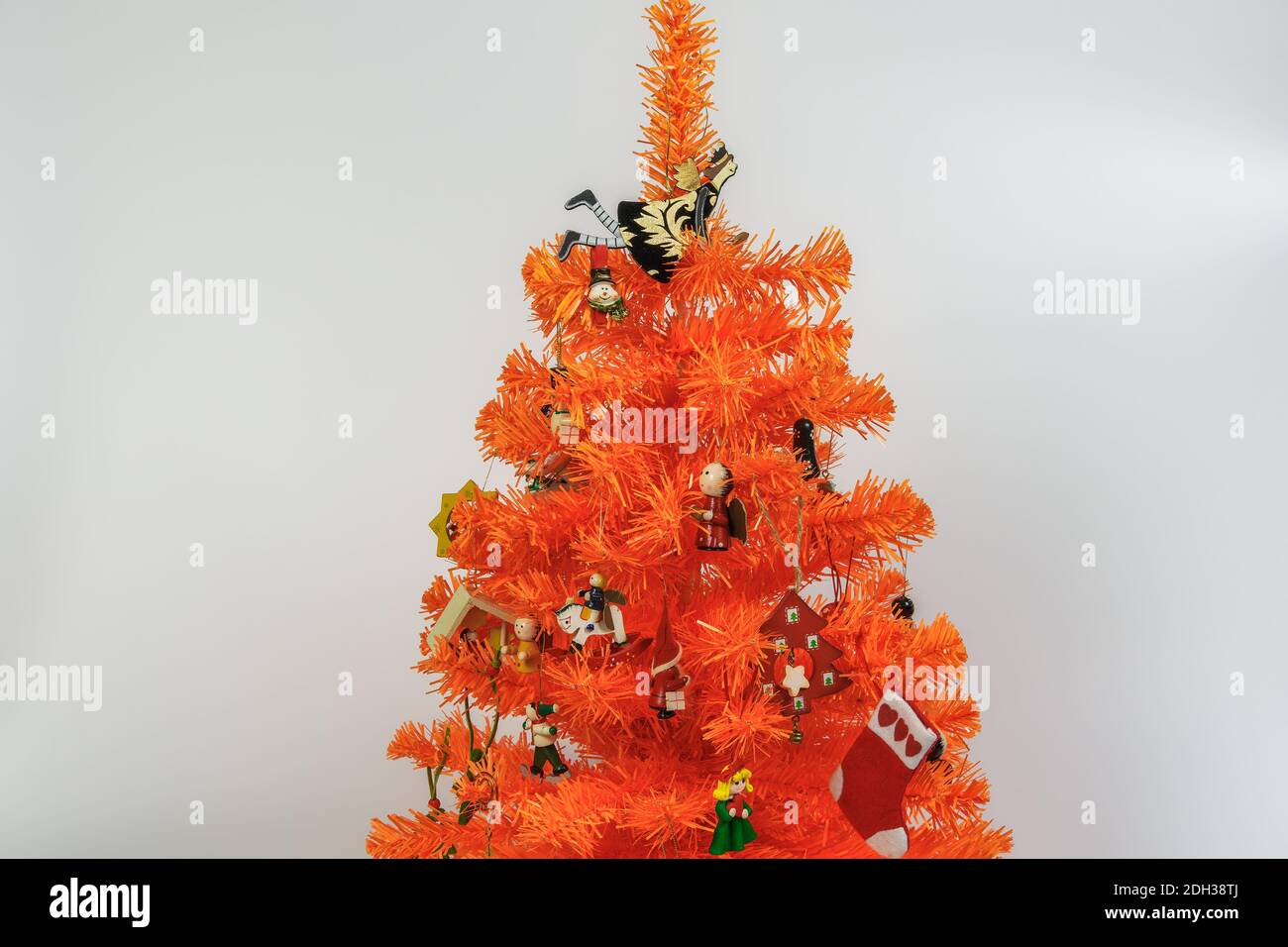 Artificial orange Christmas tree with ornaments against white background. Wooden miniature