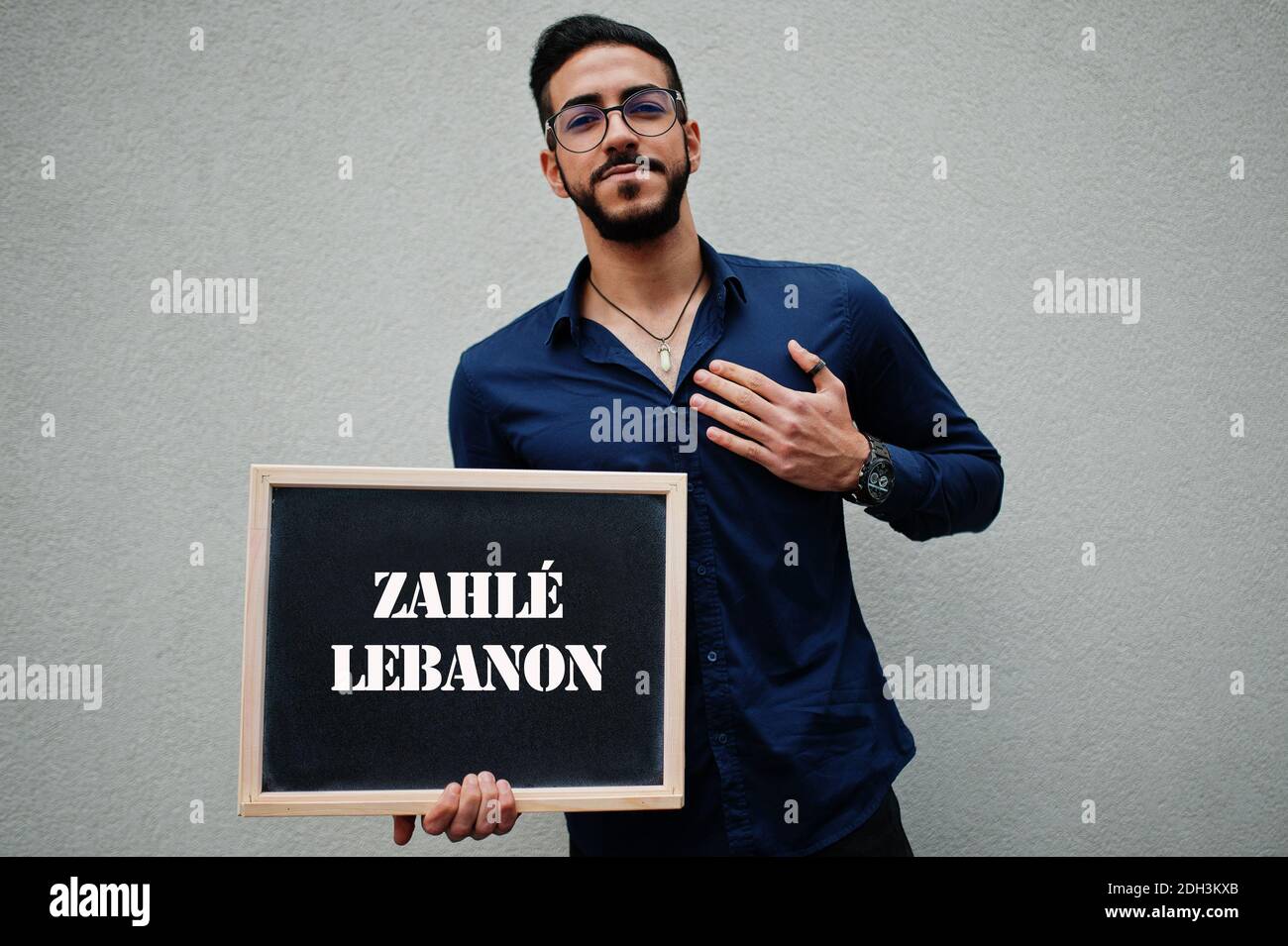 Arab man wear blue shirt and eyeglasses hold board with Zahle Lebanon inscription. Largest cities in islamic world concept. Stock Photo