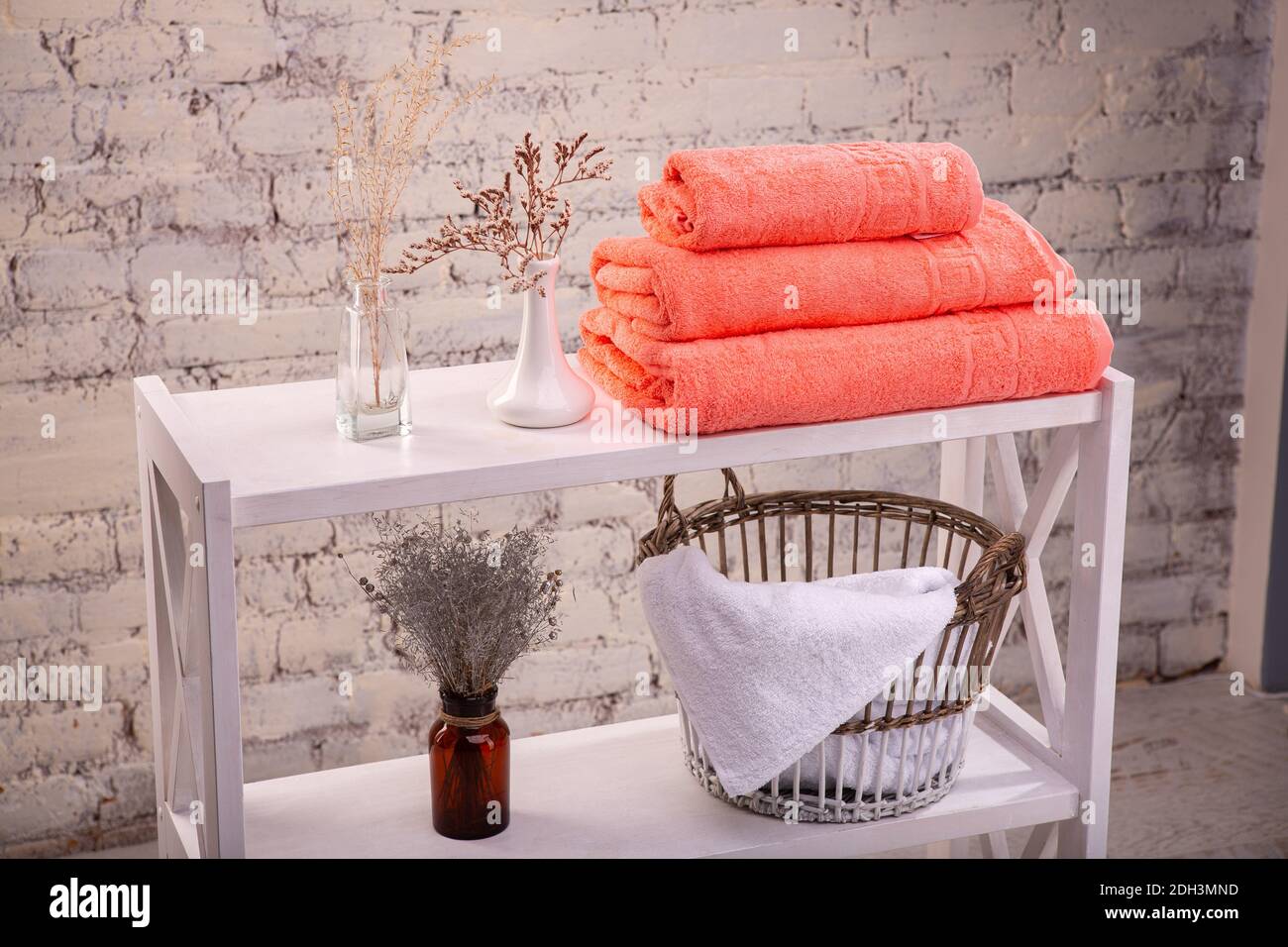Rack with a stack of three peach color towels and baskets with clean white towels and toilet decor near a brick wall. Shelf with terry towels and Stock Photo Alamy