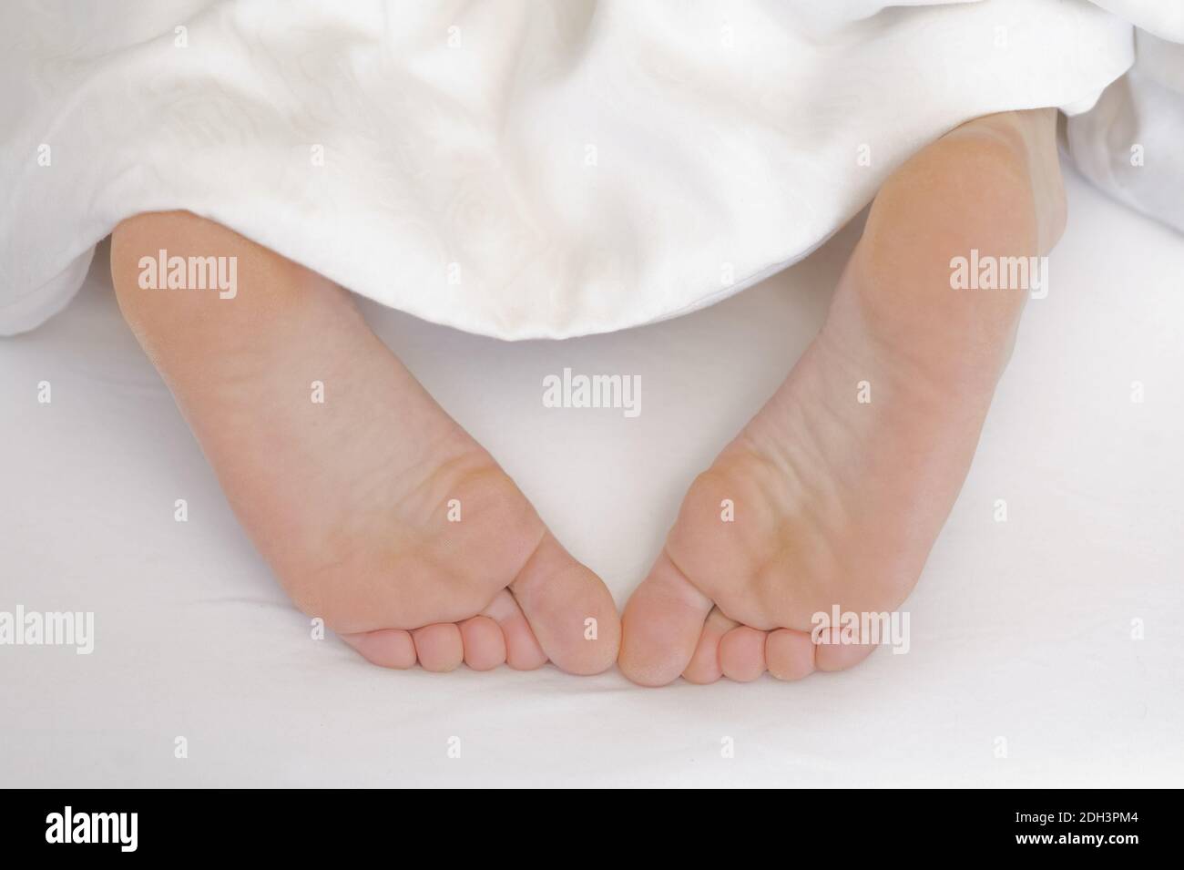25 -30 jährige Frau schläft im Bett, zeigt ihre Füsse, MR:Yes Stock Photo