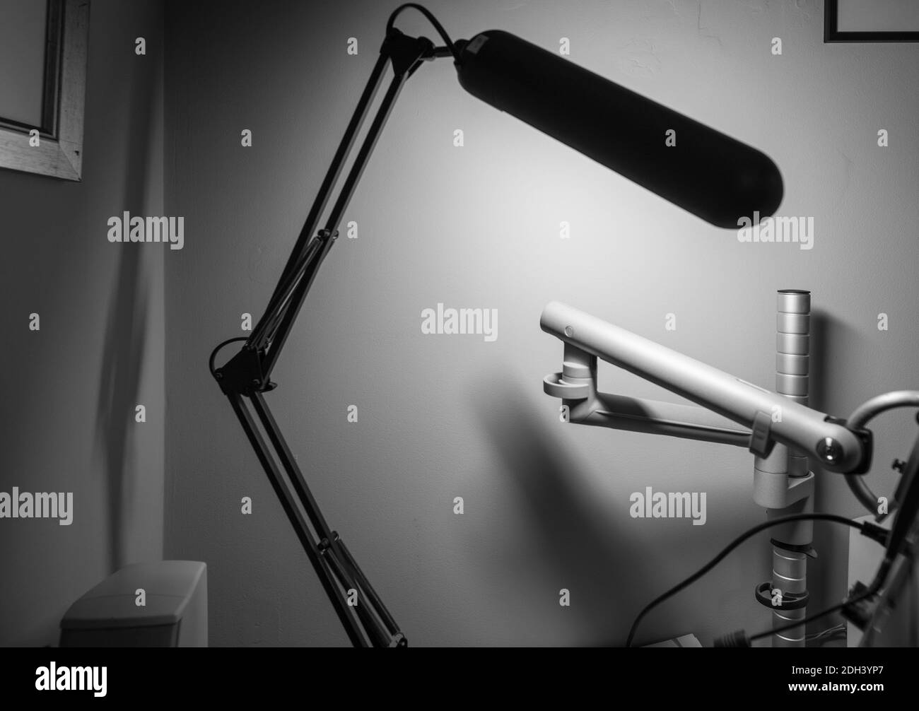 Black and white monochrome image of articulated desk lamp with black arms in foreground blur and articulated monitor stand Stock Photo