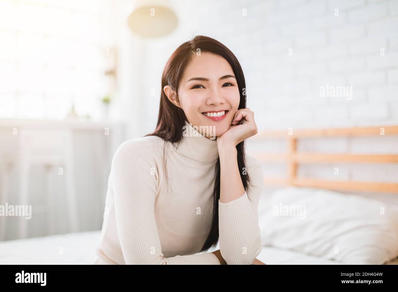 Young beautiful woman smiling and sitting on bed at home Stock Photo