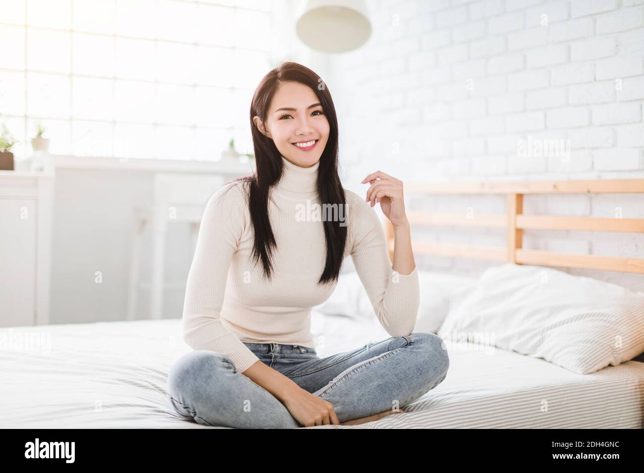 Young beautiful woman smiling and sitting on bed at home Stock Photo