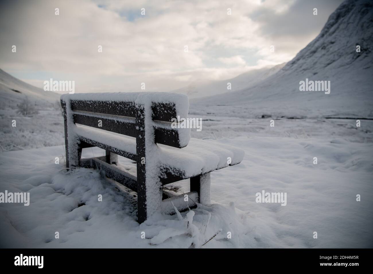 Lone bench laden in snow sits at the foot of the mountains in Glencoe, Bonnie Scotland at its wintery best. Stock Photo