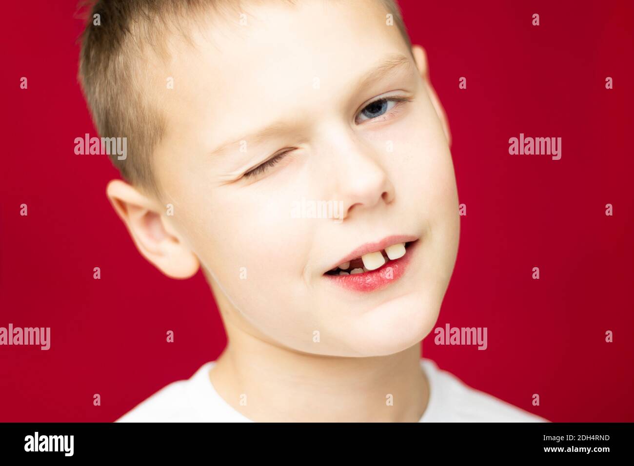 Winking teen boy 7-10 in white t-shirt on red background Stock Photo