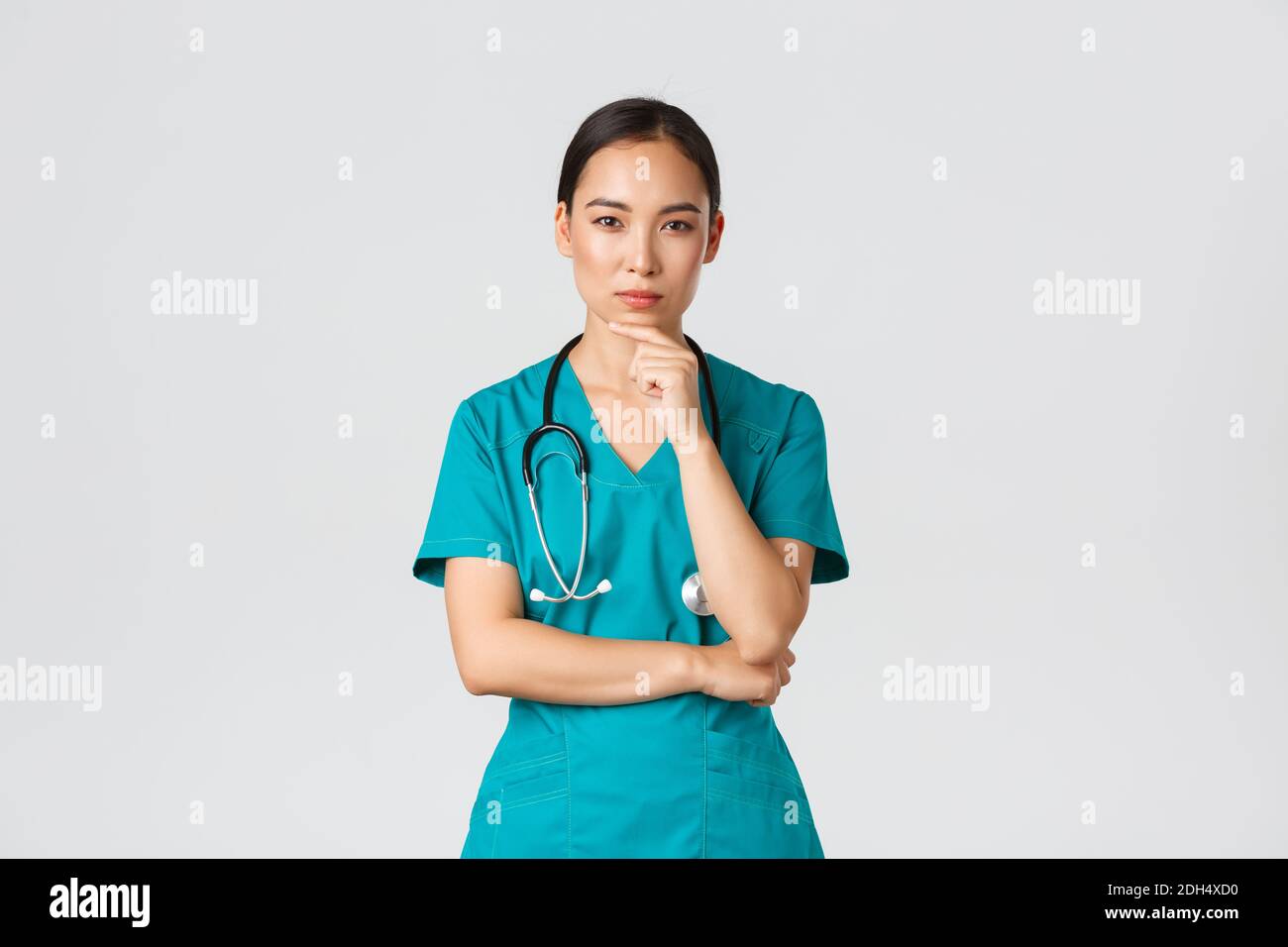Covid-19, healthcare workers, pandemic concept. Thoughtful female doctor, asian nurse in scrubs looking curious at camera, think Stock Photo