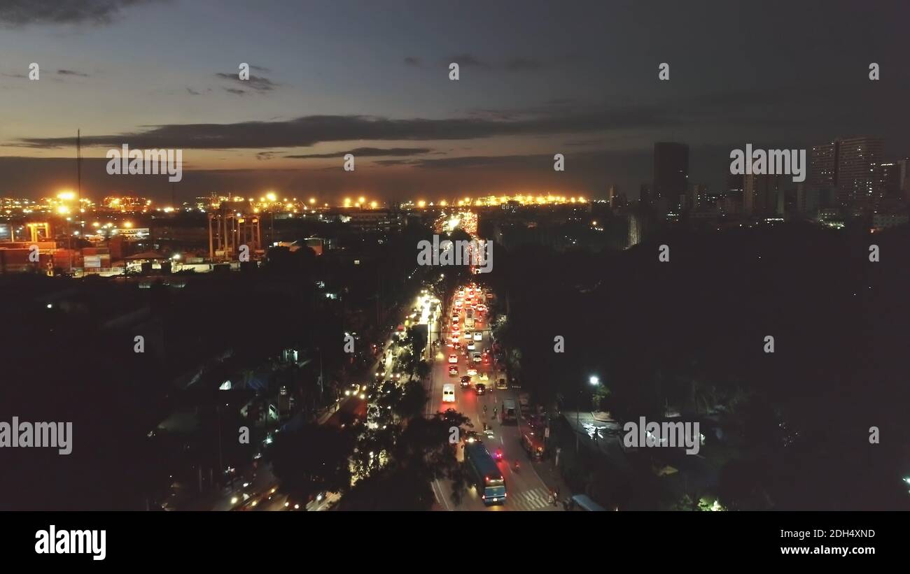 Night traffic road closeup aerial. Cars and trucks drives at modern buildings and skyscrapers at twilight. Illuminated cityscape of metropolis town of Manila, Philippines, Asia Stock Photo