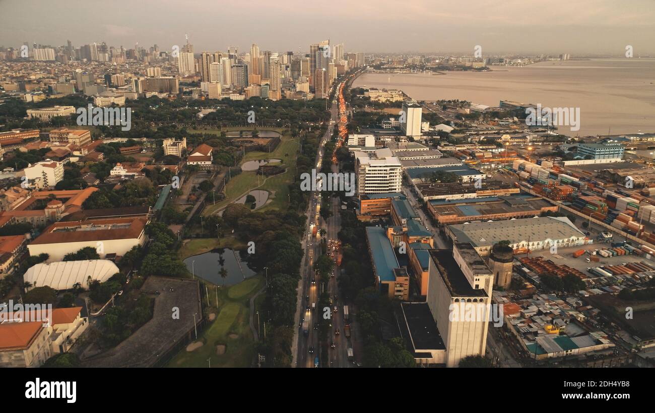 Sunset cityscape with designed park and ponds at ocean bay aerial. Port town of Manila at summer evening. High skyscrapers, block buildings, houses. Modern architecture landmark of business center. Stock Photo